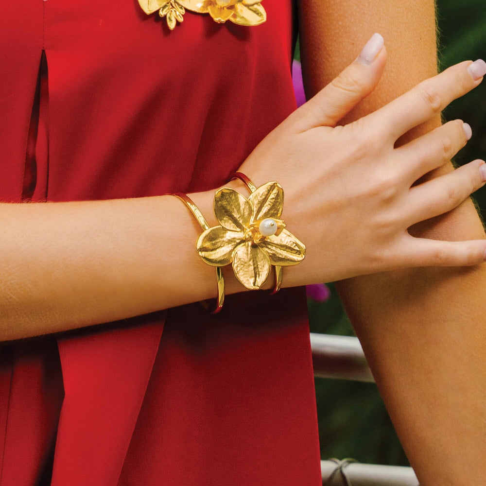 Risis 1974 Phalaenopsis Cuff Bangle - A golden bracelet shaped like a large, textured flower with a pearl center adorns a wrist; paired with a red garment.