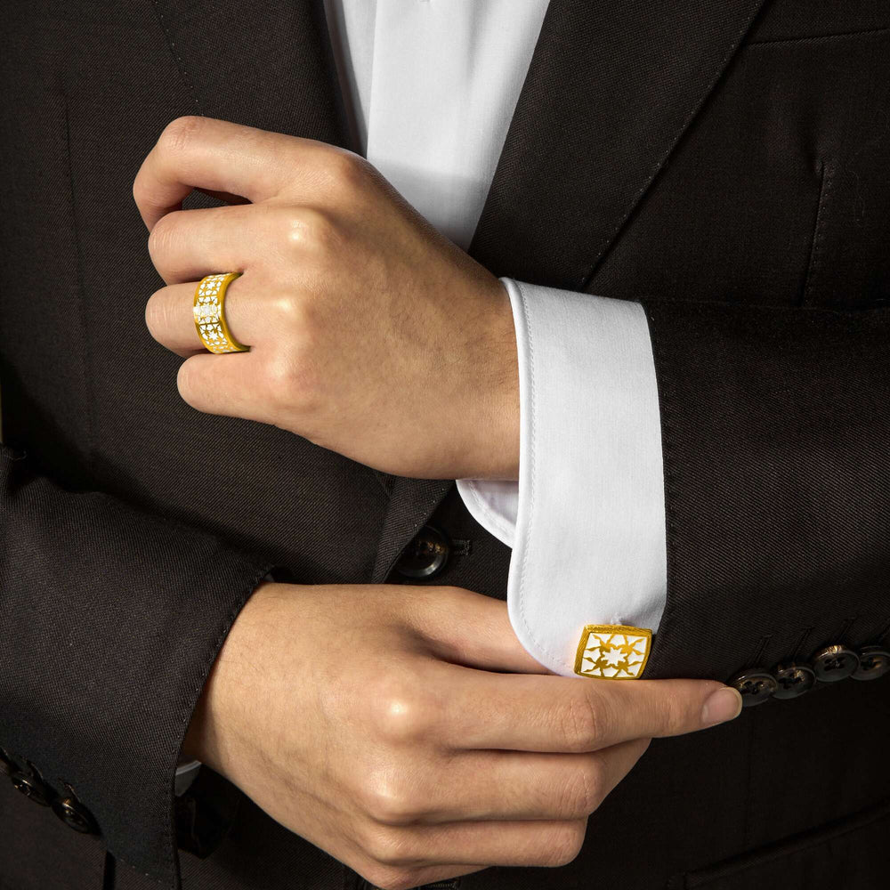 Risis Peranakan Orchid With White Enamel Cufflinks - A hand, adorned with a chunky gold ring set with small diamonds, adjusts a white cufflink with a golden geometric design on a crisp white shirt sleeve.