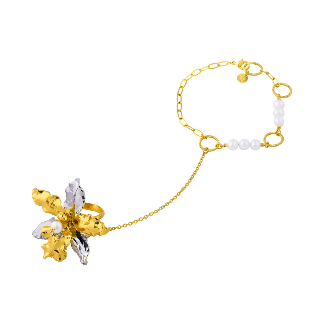 Risis 1974 Odontoglossum Hand Chain - A gold-toned bracelet features a textured, metallic flower with silver and gold petals, connected to a chain interspersed with lustrous white beads.