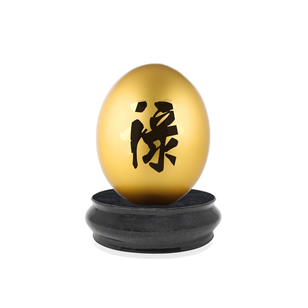Risis Auspicious Egg II - Lu (Large) - A golden egg with intricate black calligraphy, resting on a dark circular base, artistically isolated against a white backdrop.