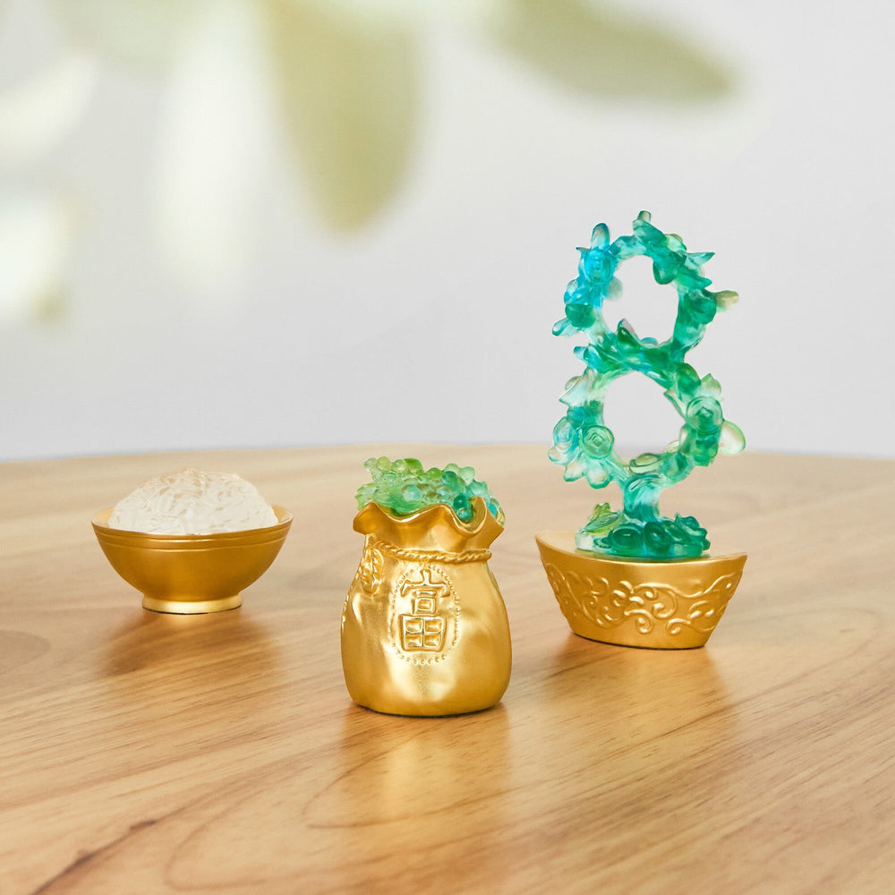 Risis Auspicious Fortune Bag with Liu Li - Three ornamental objects are displayed: a translucent blue-green floral sculpture atop a golden base; a golden pouch with embossed textures; and a golden bowl cradling white content.