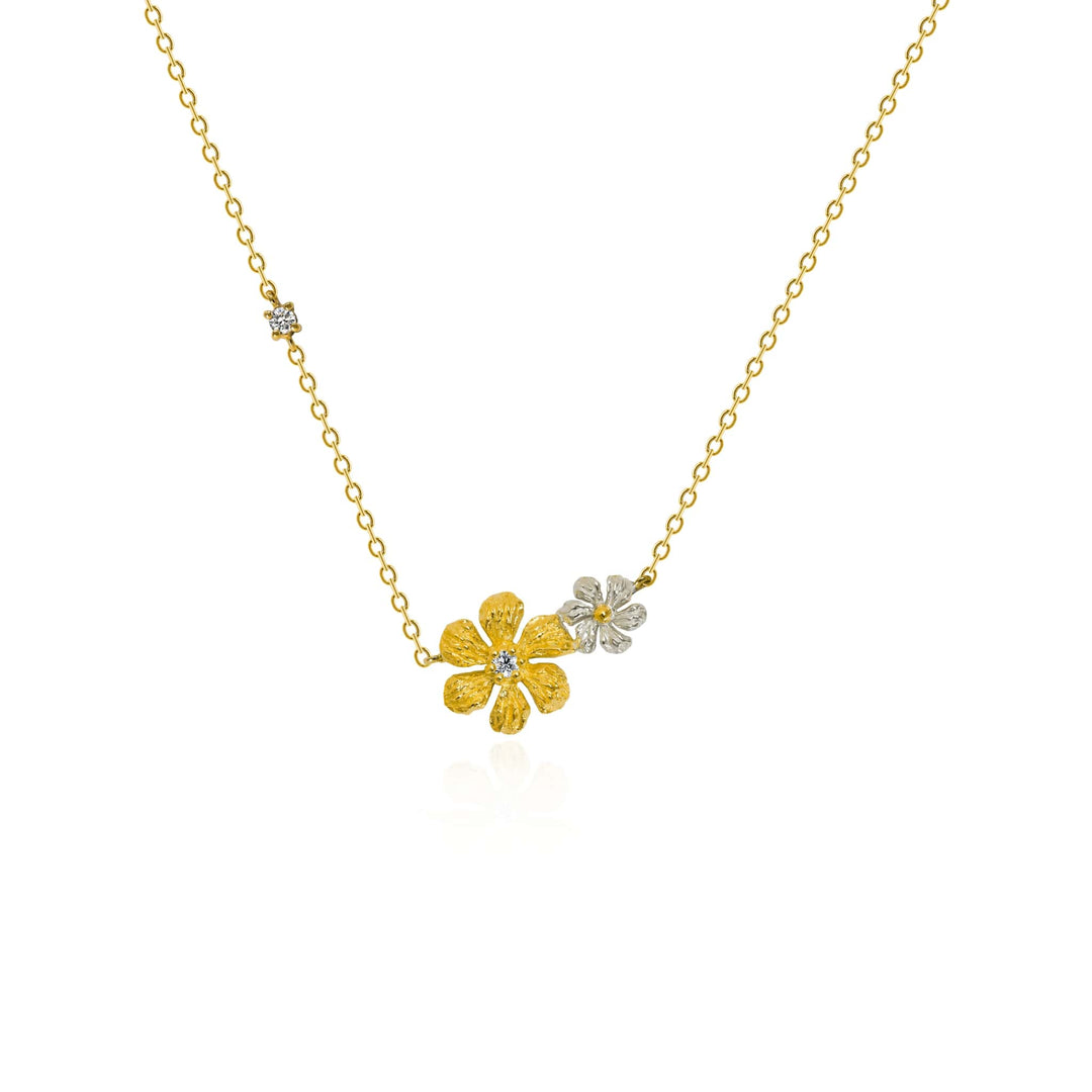 Risis Enchanted Jasmine Necklace II - A delicate gold necklace showcases three floral pendants—two gold, one silver—each with a sparkling gem at the center, arranged asymmetrically against a plain backdrop.