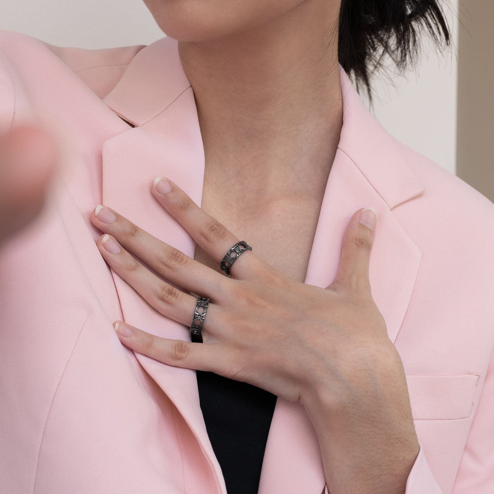 Risis Entwined Rattan Ring (BRH) - A person is wearing ornate silver rings with dark inlays on multiple fingers, touching a soft pink blazer lapel.