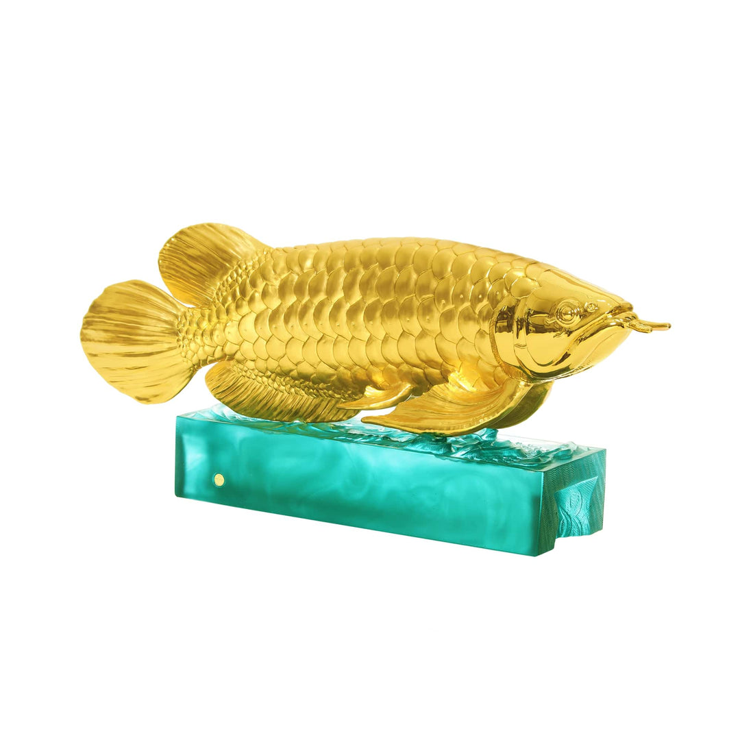 Risis Majestic Arowana - A golden fish sculpture with intricate scales details resting on a turquoise, reflective base, creating an artistic display of contrast and opulence.