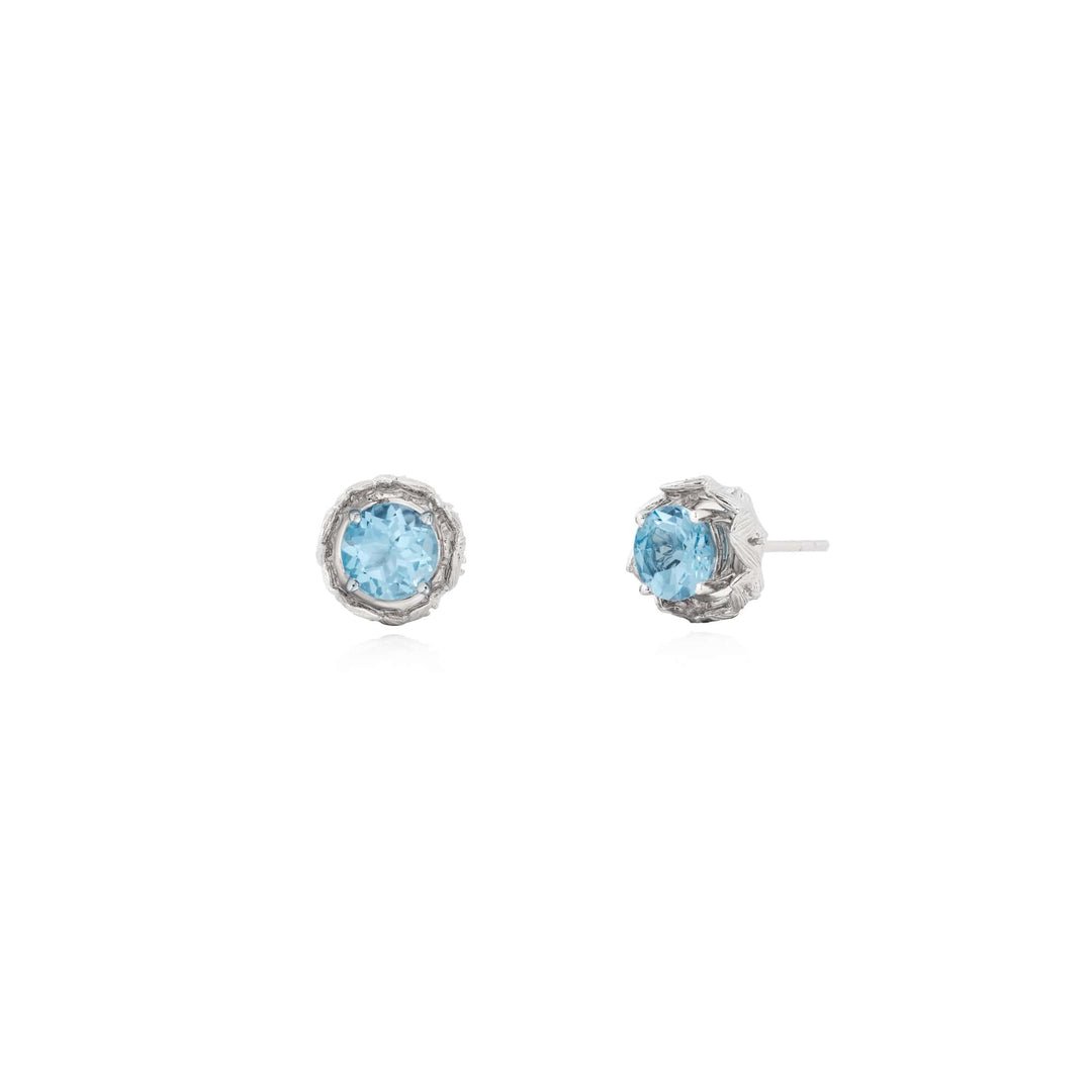 Risis Midori Earrings With Sky Blue Topaz (RH) - A pair of silver-colored earrings with intricate detailing, showcasing central light blue gemstones set within textured, ornate mounts, reflecting elegance and artistry.