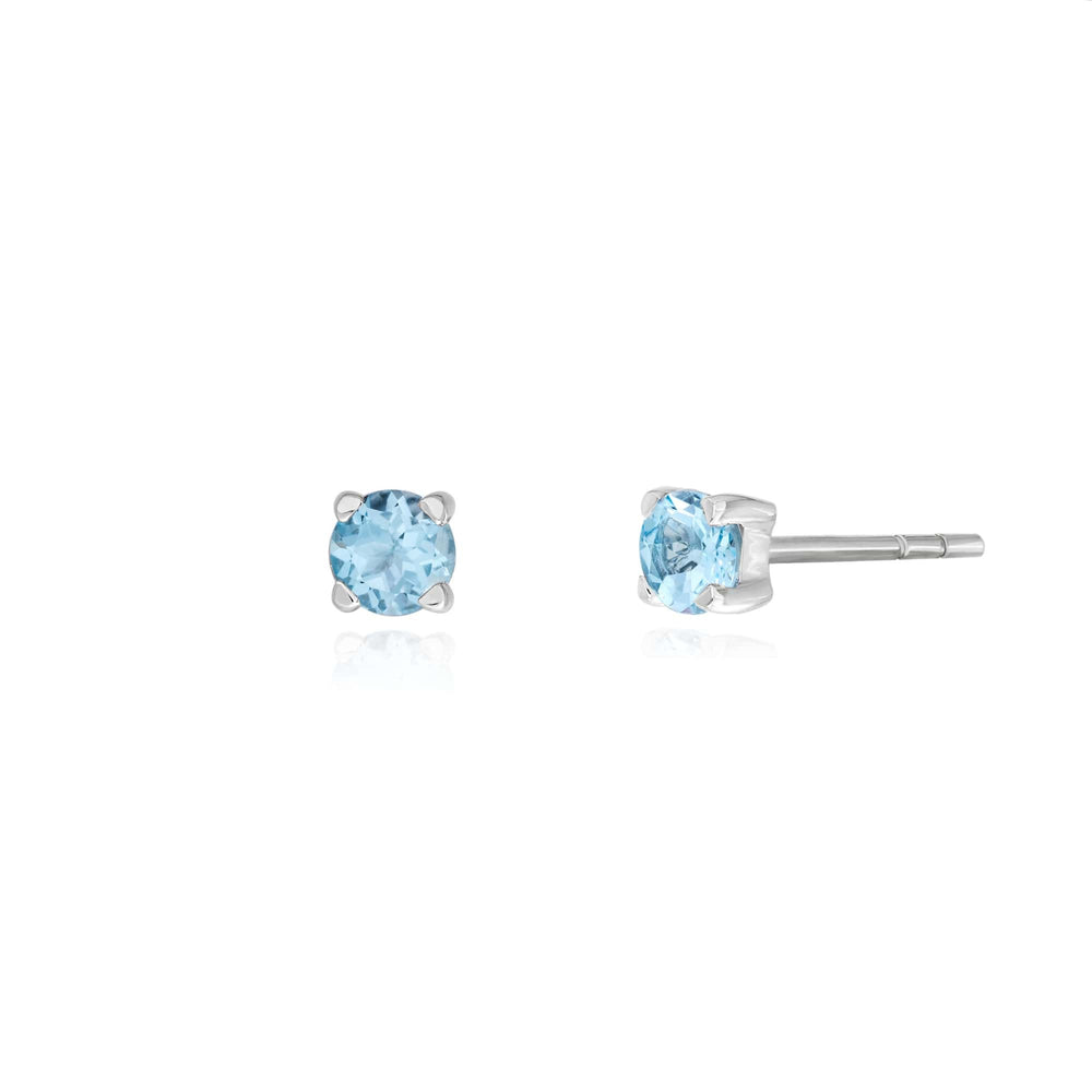 Risis Midori Earrings With Sky Blue Topaz (RH) - A pair of stud earrings featuring round-cut, pale blue gemstones set in a four-prong silver setting. They exude simplicity and elegance.