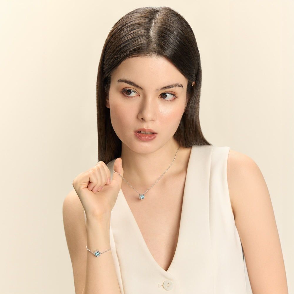Risis Midori Necklace With Sky Blue Topaz (RH) - A woman showcases a delicate silver necklace with a blue gem pendant and a matching bracelet, emphasizing the shimmer and elegance of the jewelry.