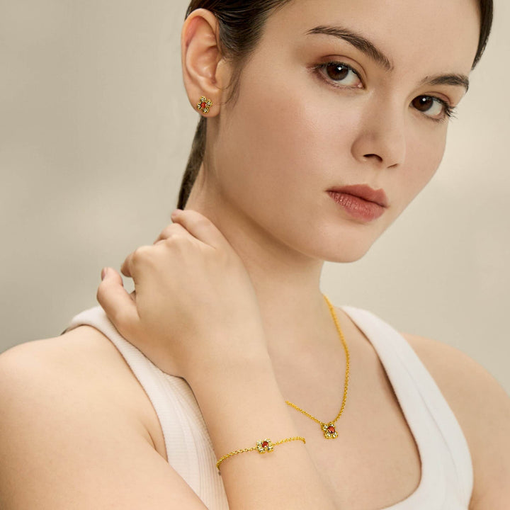 Risis Petite Peranakan Kebaya Earrings With Garnet - A woman is adorned with gold jewelry featuring red and green stones: stud earrings, a delicate bracelet, and a matching necklace, conveying elegance.
