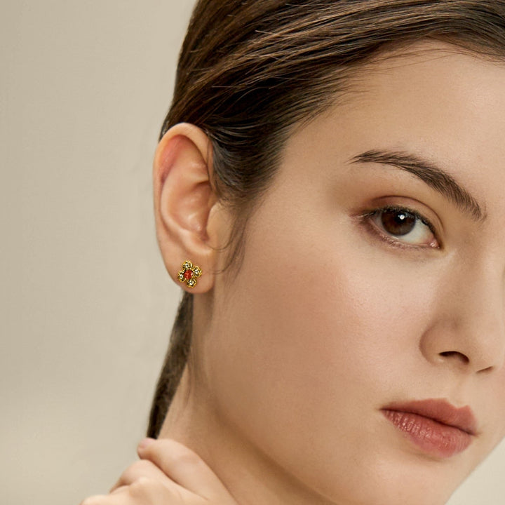 Risis Petite Peranakan Kebaya Earrings With Garnet - A gold flower-shaped earring with red gem petals adorns the ear of a woman with sleek hair.