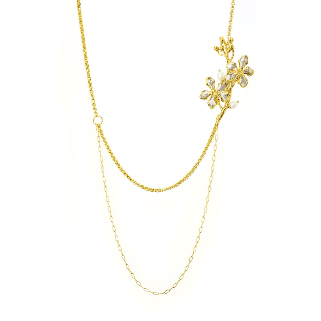 Risis Vanda Symphony Necklace with Pearls - A delicate gold necklace features a glittering branch with crystal flowers and pearls, highlighting its intricate elegance against a plain backdrop.