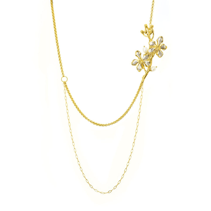 Risis Vanda Symphony Necklace with Pearls - A delicate gold necklace features a glittering branch with crystal flowers and pearls, highlighting its intricate elegance against a plain backdrop.