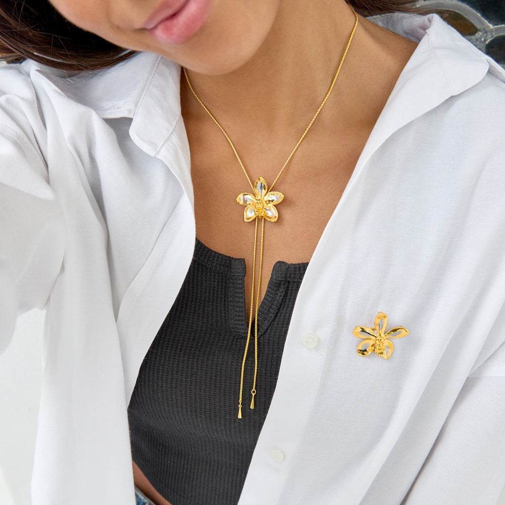 Risis Aeridovanda Vieng Ping Orchid Brooch/Pendant (PG) - A person is wearing a gold necklace with a floral pendant and matching brooch, contrasting against a white shirt and black top.