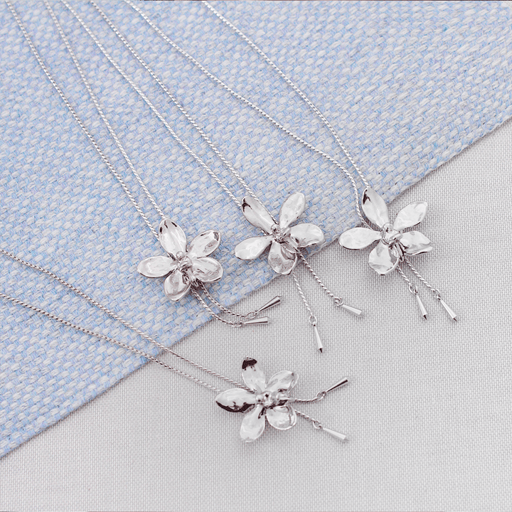Risis Aeridovanda Vieng Ping Orchid Slider Necklace (P) - Four silver necklaces with floral pendants, featuring a design resembling five-petaled flowers, each with a textured finish, displayed on a textured surface.