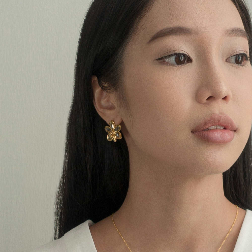 Risis Ascocenda Sagarik Gold Orchid Earrings (PG) - A golden floral earring with lustrous accents dangles delicately from a woman's ear, exuding elegance and simplicity.