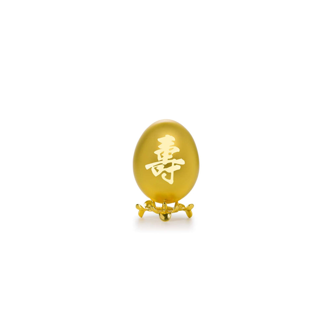 Risis Auspicious Egg - Shou (Small) - A smooth, amber-colored oval gemstone with an intricately carved Chinese character, displayed on a delicate golden stand.