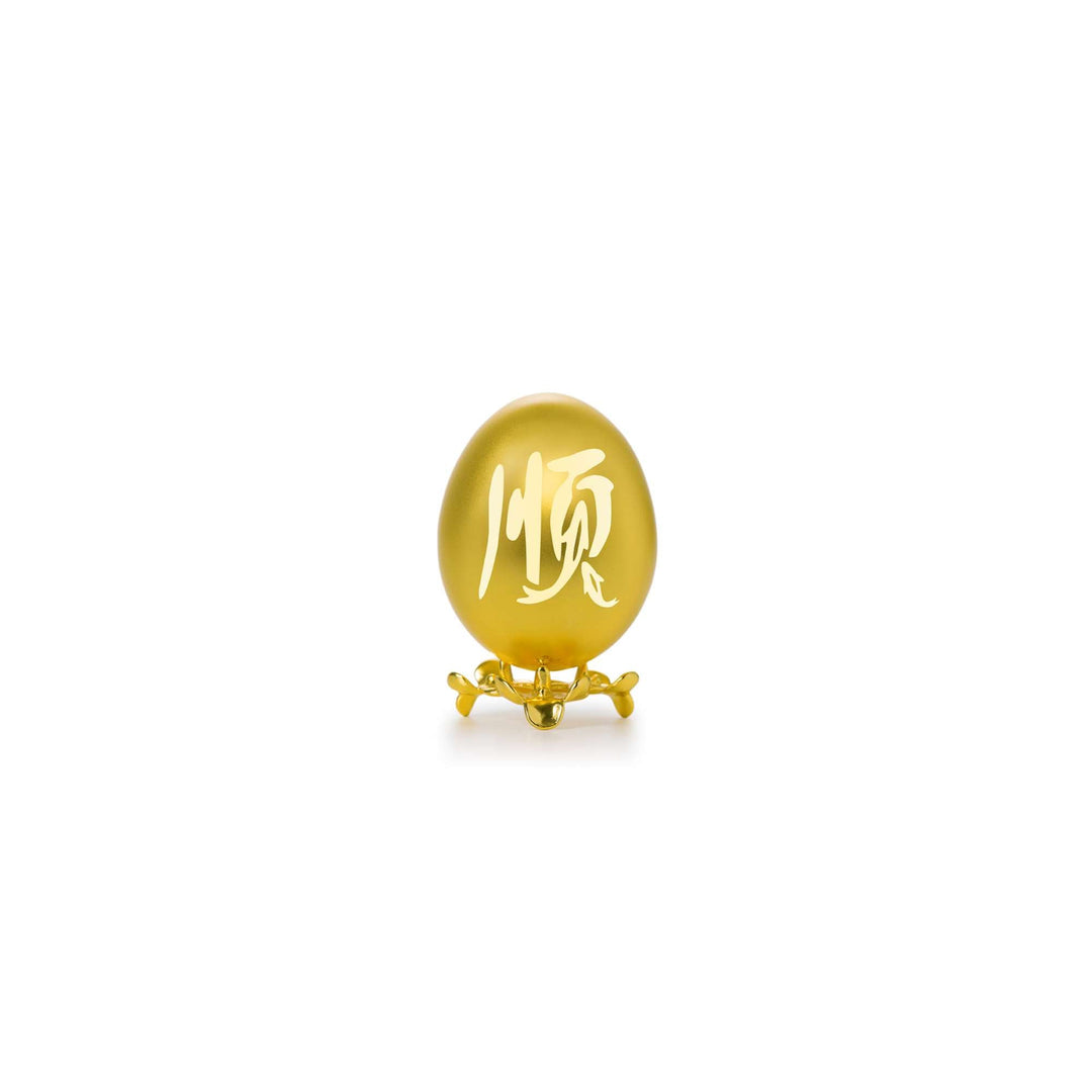 Risis Auspicious Egg - Shun (Small) - A matte golden egg-shaped object with elegant white calligraphy, displayed on a tiny, ornate gold stand.