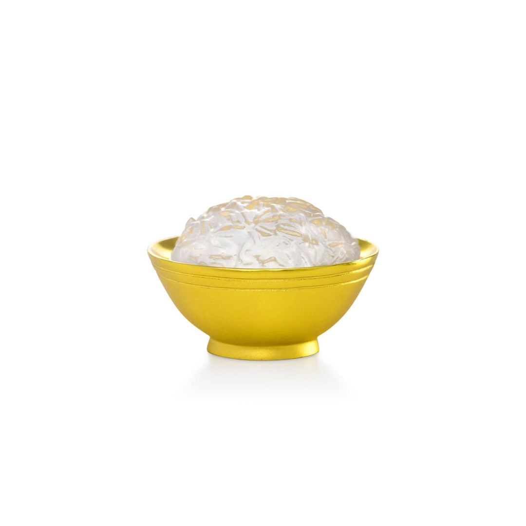 Risis Auspicious Rice Bowl - A gold-colored bowl cradles an intricately textured, translucent white object resembling an ornamental piece or a pearl-like gem.