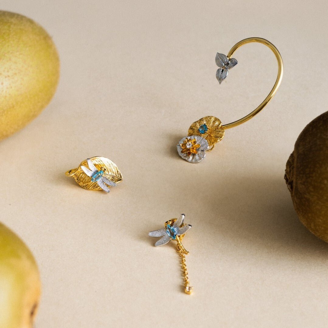 Risis Botanique Water Lily Ear Cuff - Gold jewelry pieces with delicate dragonfly and floral motifs, adorned with sparkling accents, are artistically displayed, invoking a sense of elegance and nature-inspired design.