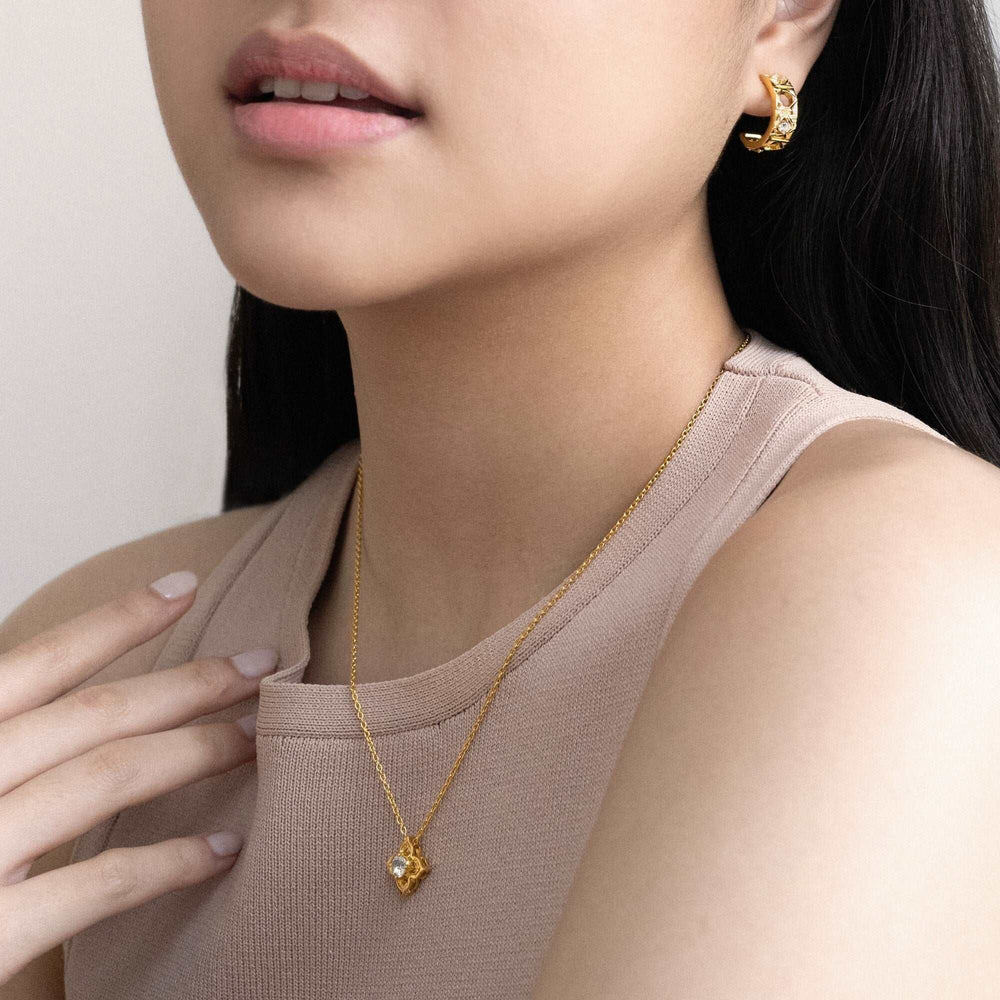 Risis Entwined Rattan Earrings - A person's hands adorned with elegant jewelry; gold rings set with clear gems on one hand and silver bands with intricate designs on the other, contrast against a white garment.