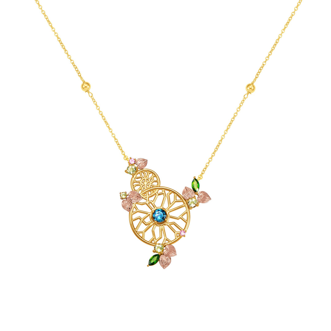 Risis Garden Odyssey Kaleidoscope Necklace - A delicate gold necklace with a geometric circular pendant adorned with small pink and green leaves, multicolored gems, and a prominent blue stone at its center.
