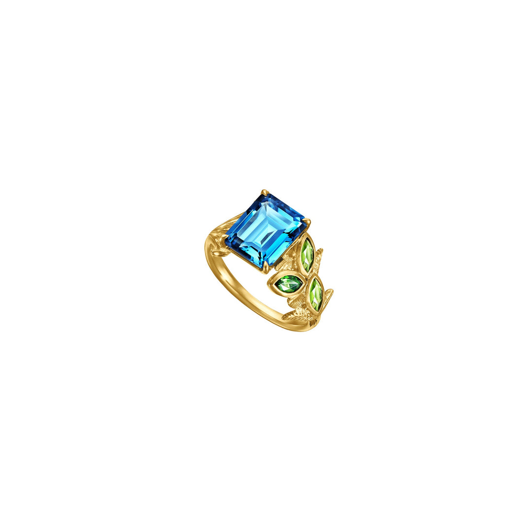 Risis Garden Odyssey Medley Ring - A golden ring featuring a prominent rectangular blue gemstone, flanked by leaf-shaped green gems, evokes elegance.