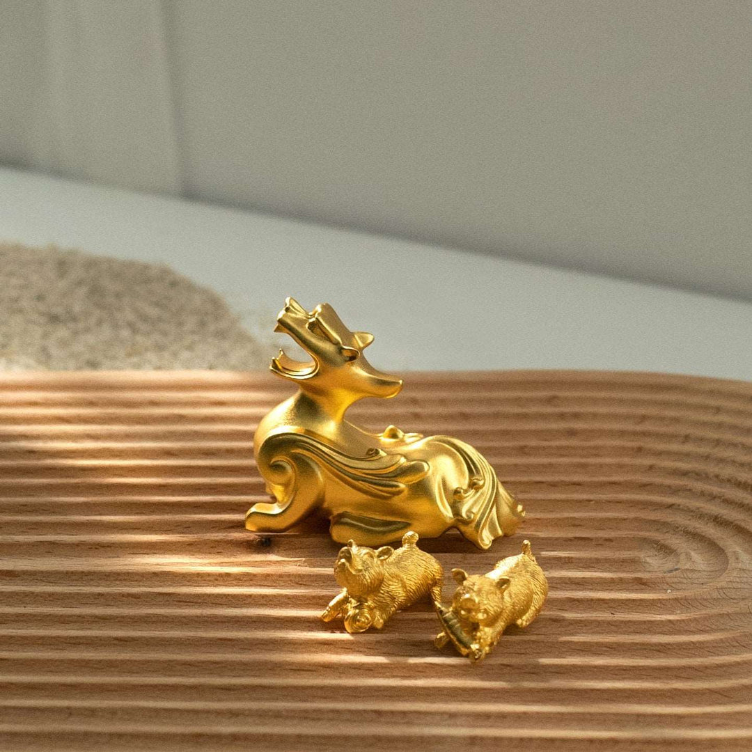 Risis Golden Miniature Pixiu - A glossy golden sculpture of a stylized deer and two small bears, reflecting sunlight, positioned on a ribbed wooden surface.