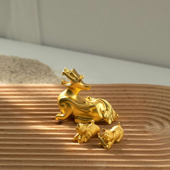 Risis Golden Miniature Pixiu - A glossy golden sculpture of a stylized deer and two small bears, reflecting sunlight, positioned on a ribbed wooden surface.