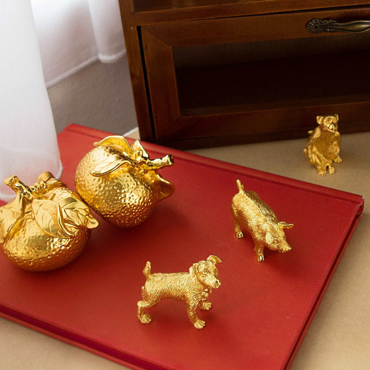 Risis Golden Tangerines - Golden figurines of fruit and animals, intricately textured, rest on a deep red surface; the objects shimmer with a polished, ornate appearance.
