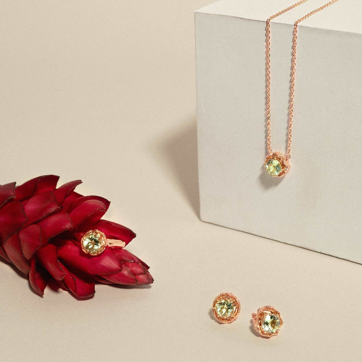 Risis Midori Earrings with Prasiolite (RG) - A rose gold necklace with a delicate chain and a central, round, pale green gemstone pendant is displayed. Matching stud earrings with similar green gemstones are beside it.