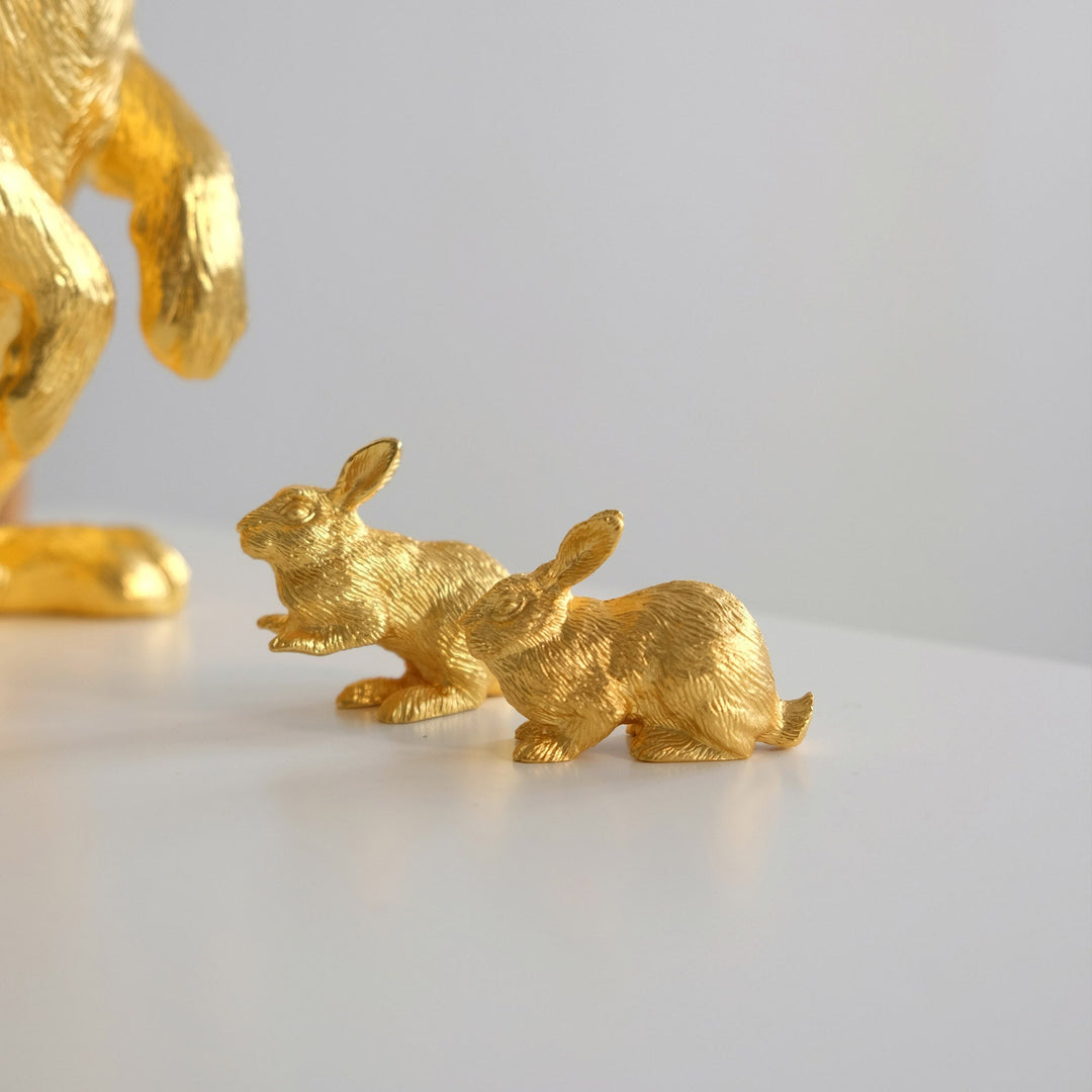 Risis Mini Orientals - Rabbit - Two small, textured, golden rabbit figurines are arranged in a line as if hopping forward, gleaming with a metallic luster.
