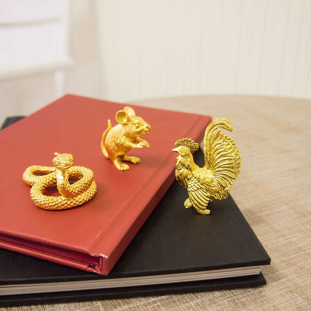 Risis Mini Orientals - Rat - Golden figurines—a coiled snake, a mouse, and a rooster—sit atop two stacked books, showcasing intricate textures and a lifelike appearance.