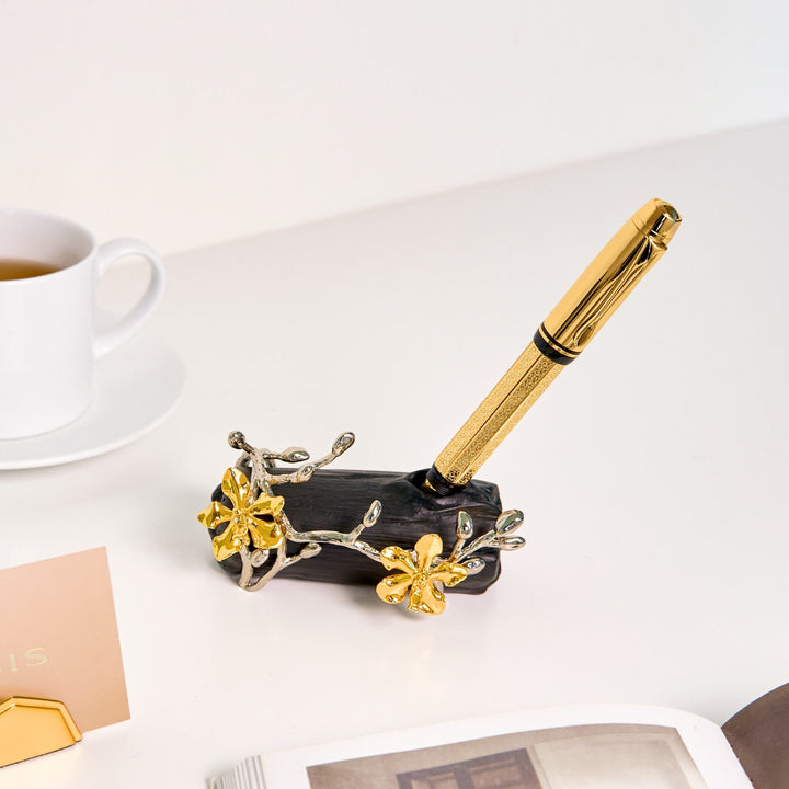 Risis Orchid Spiral Charcoal Pen and Name Card Holder - A golden pen with textured detailing rests on a black stand adorned with golden and silver blossoms and vines, displaying elegance and functionality.