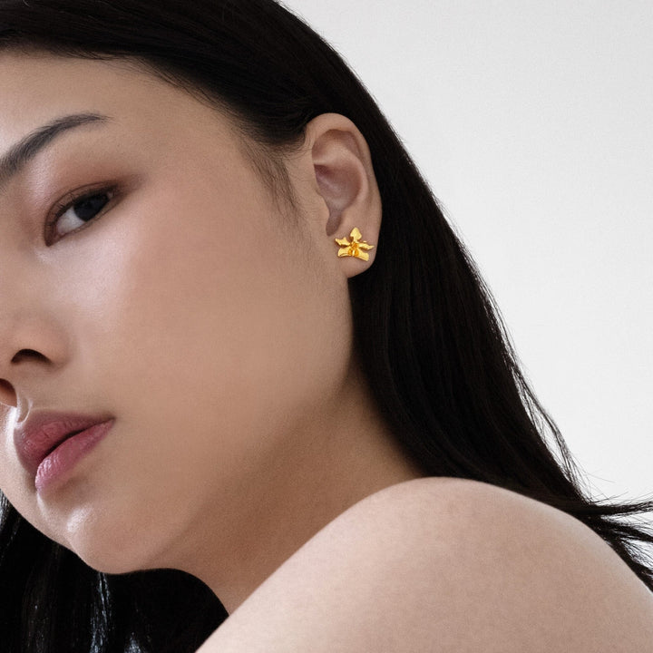 Risis Orchid Spiral Earrings - A person's wrist is adorned with a silver cuff bracelet with golden flower designs, and their fingers showcase rings with similar floral motifs.