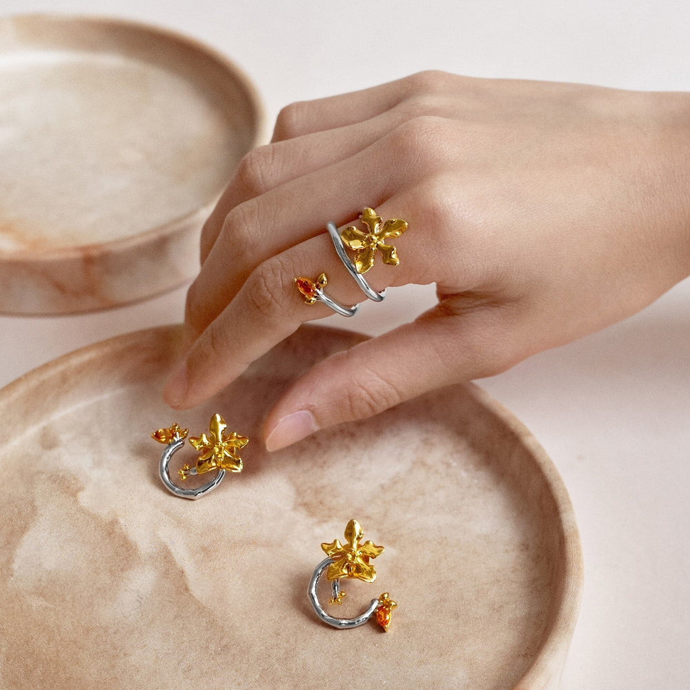 Risis Orchid Spiral Ring - Silver and gold-toned metal flowers decorate artistic objects, displaying intricate designs with lustrous, eye-catching finishes on a neutral surface.
