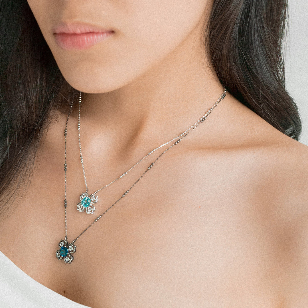 Risis Peranakan Kebaya Necklace (RH) with Sky Blue Topaz - A woman is wearing two layered silver necklaces with green and blue flower-shaped pendants; they are delicate and add a touch of elegance.