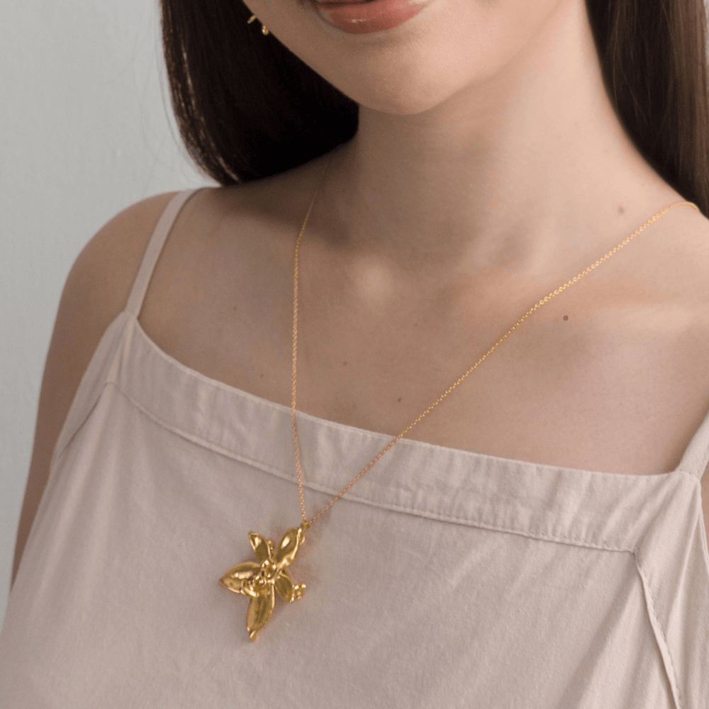 Risis Phalaenopsis Cornu Cervi Orchid Necklace (G) - A delicate gold necklace with an ornate bee pendant adorns a person's neck, resting against a pale top.