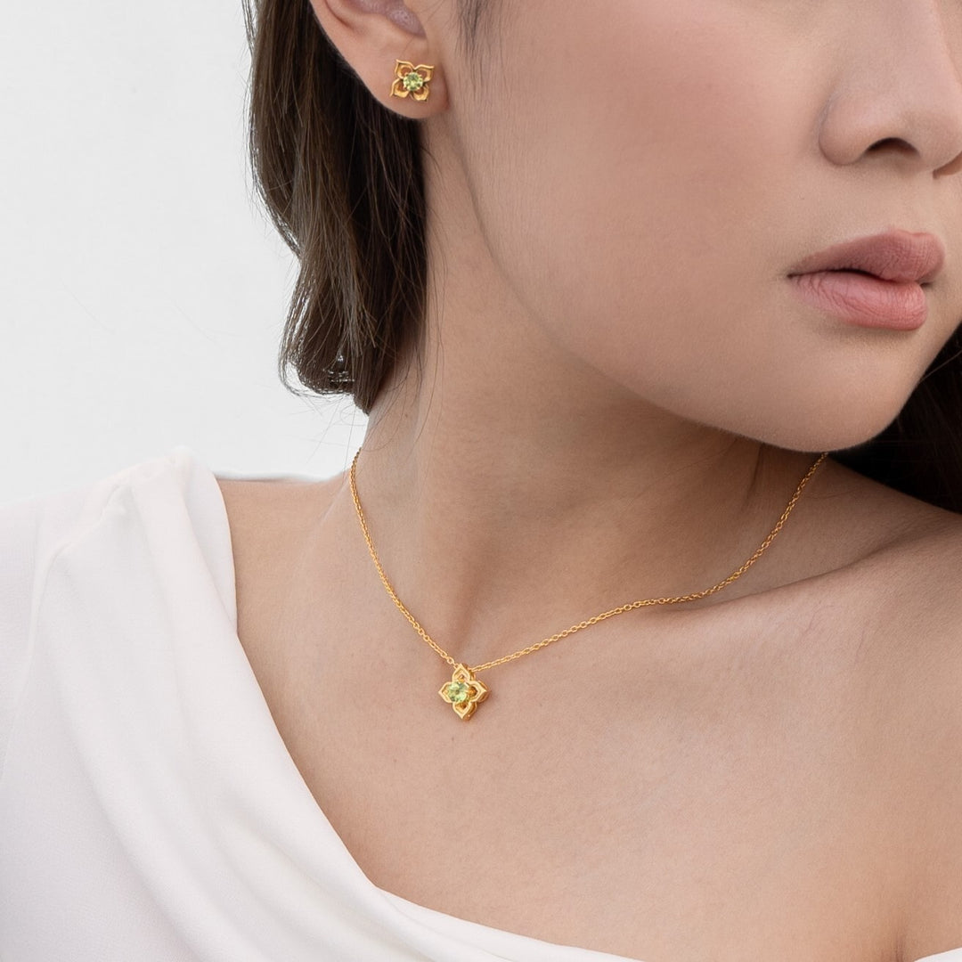 Risis Timeless Peranakan Earrings With Peridot - A person is wearing a gold necklace with a floral pendant and matching earrings. The jewelry has intricate details and a subtle shine.