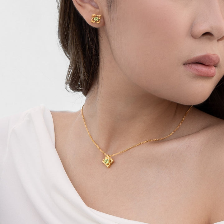 Risis Timeless Peranakan Earrings With Peridot - A person is wearing a gold necklace with a floral pendant and matching earrings. The jewelry has intricate details and a subtle shine.