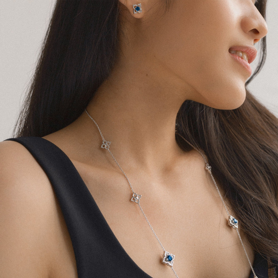 Risis Timeless Peranakan II Earrings (RH) with London Blue Topaz - A woman wears a delicate silver necklace with star-shaped pendants, each centered with blue gemstones, complemented by matching star-shaped earrings.