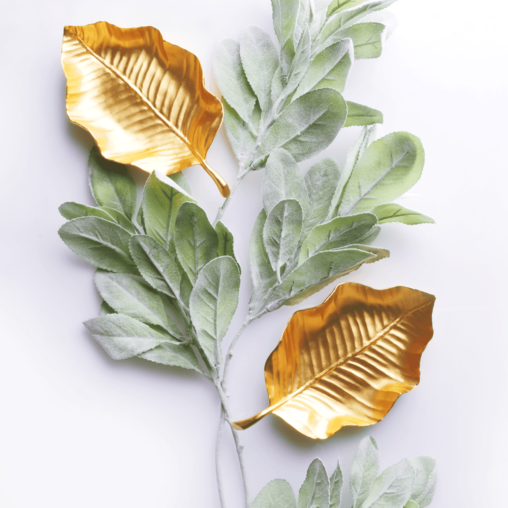 Risis Tropical Leaf Tray - Two golden metallic leaves are accompanied by branches of delicate, velvety green leaves, contrasting textures and colors in an artistic arrangement.
