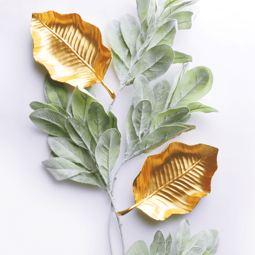 Risis Tropical Leaf Tray - Two golden metallic leaves are accompanied by branches of delicate, velvety green leaves, contrasting textures and colors in an artistic arrangement.