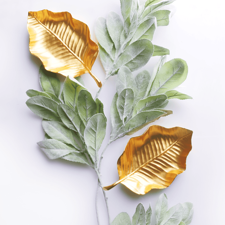 Risis Tropical Leaf Tray - Two golden metallic leaves are accompanied by branches of delicate, velvety green leaves, contrasting textures and colors in an artistic arrangement.