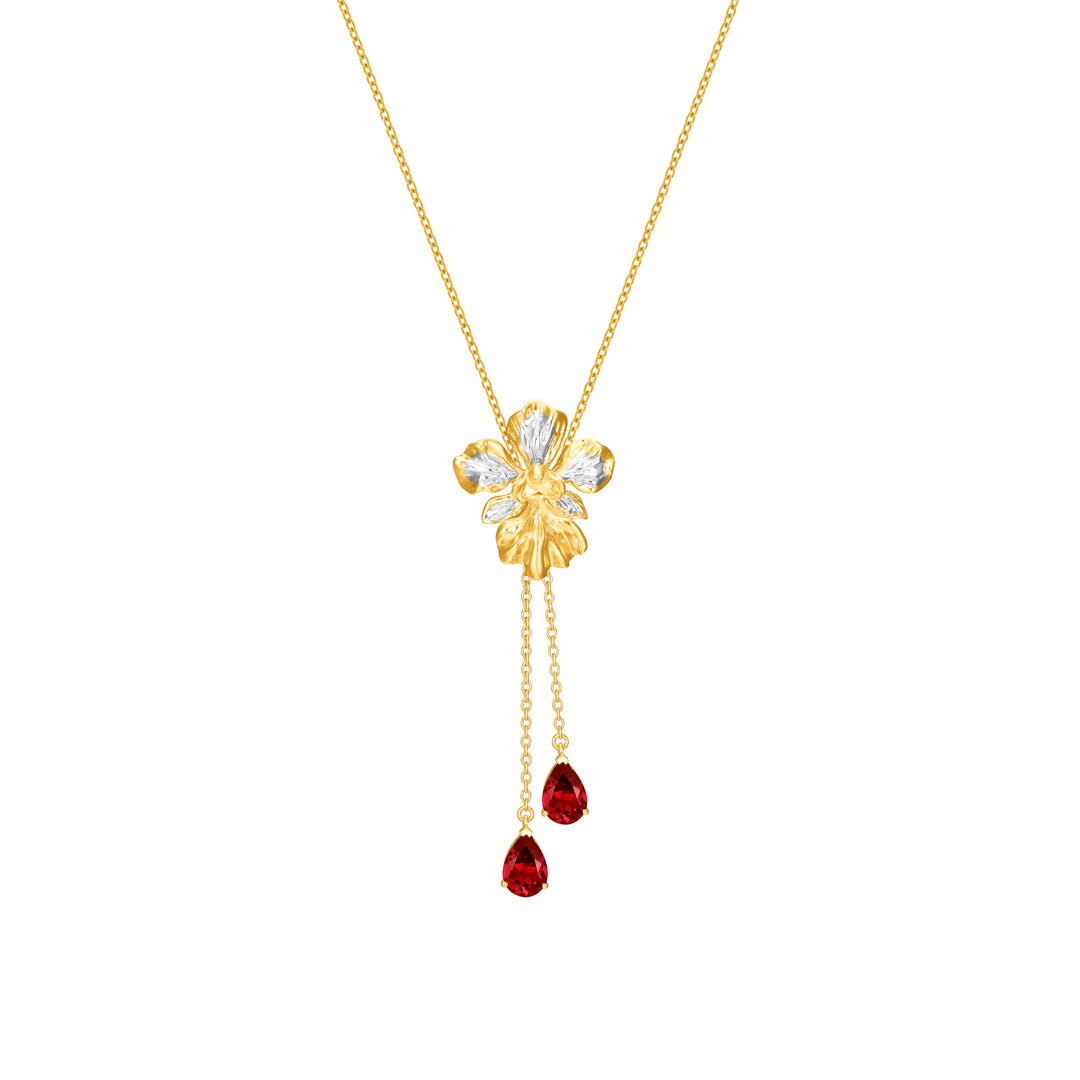 Risis Vanda Miss Joaquim Heritage Long Necklace with Garnet - A golden necklace with a floral pendant, accented by translucent petals and two dangling red teardrop gems, embodies elegance and vibrant color contrast.
