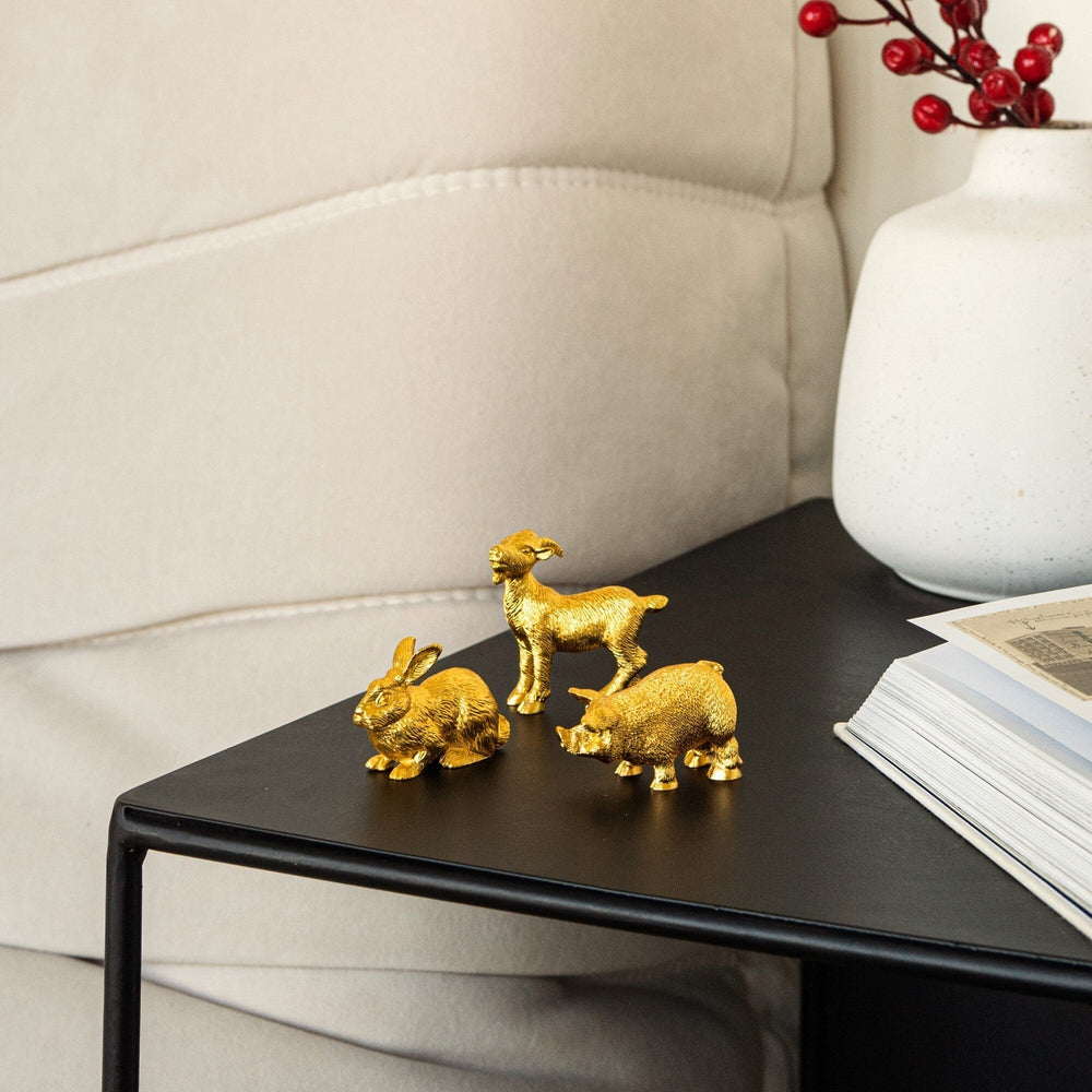 Risis Zodiac Pig Figurine - Three golden animal figurines—a rabbit and two lambs—display vibrant, lustrous textures as they rest on a flat, dark surface.