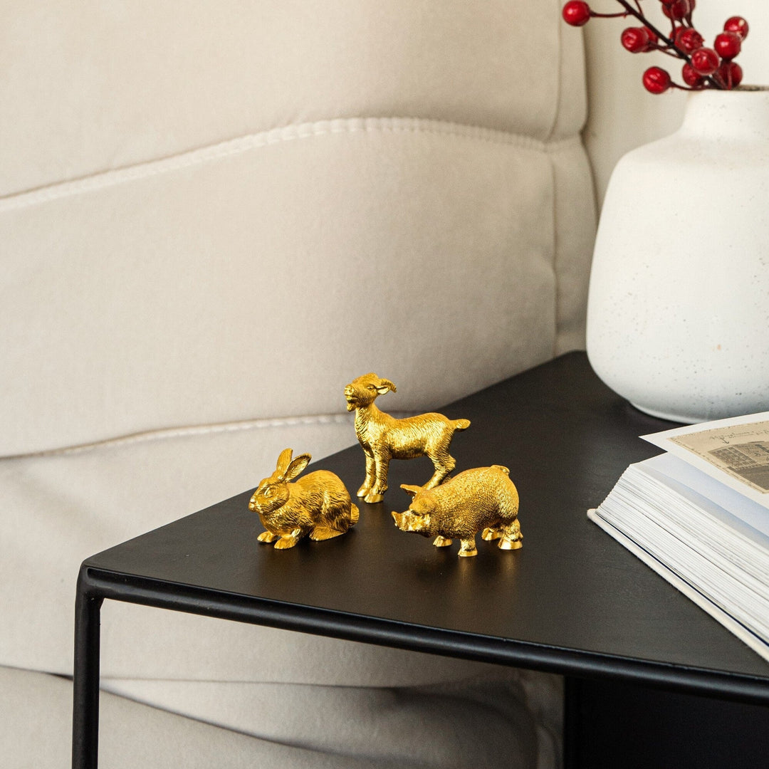 Risis Zodiac Pig Figurine - Three golden animal figurines—a rabbit and two lambs—display vibrant, lustrous textures as they rest on a flat, dark surface.