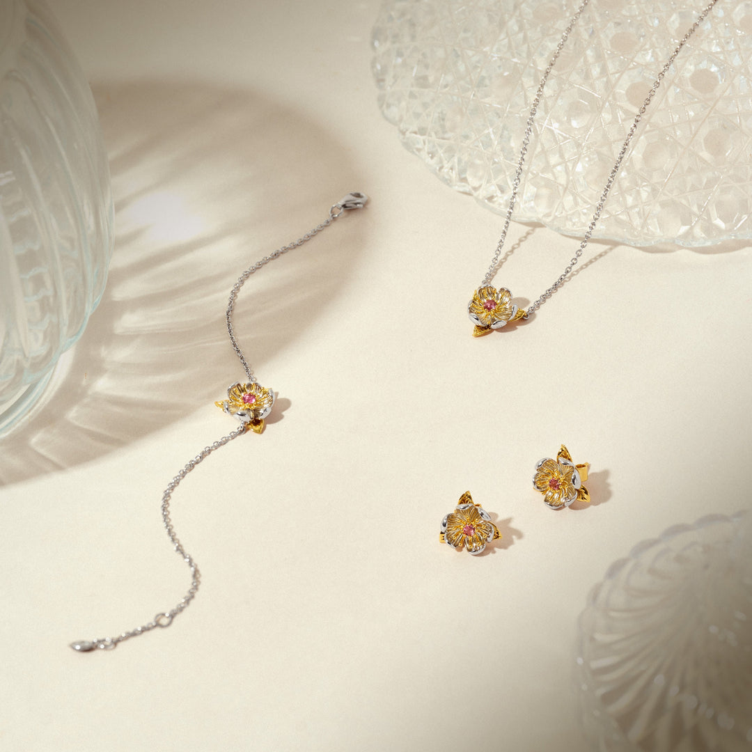 Risis Magnolia Blossom Necklace - Two silver necklaces with yellow floral pendants and matching earrings set on a beige surface, exuding elegance and delicate craftsmanship.