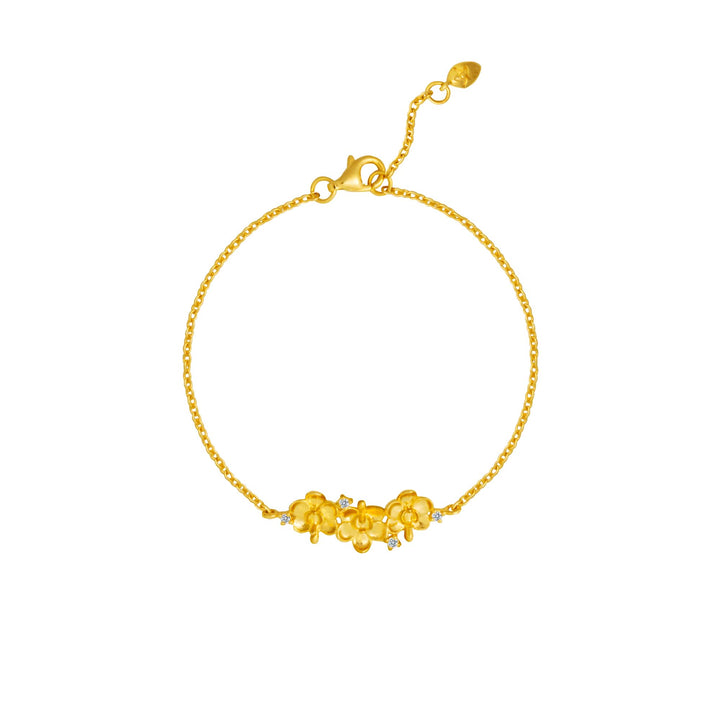 Risis Ascocenda Garden Bracelet - A golden bracelet with a delicate chain features a central decorative element of intertwined flowers, each accented with a small gem at its center.