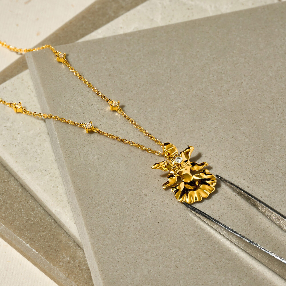 Risis 1974 Oncidium Engeline Lee Necklace - A golden necklace with a detailed sunflower pendant and small, shiny gem at its center rests delicately on a neutral-toned surface.