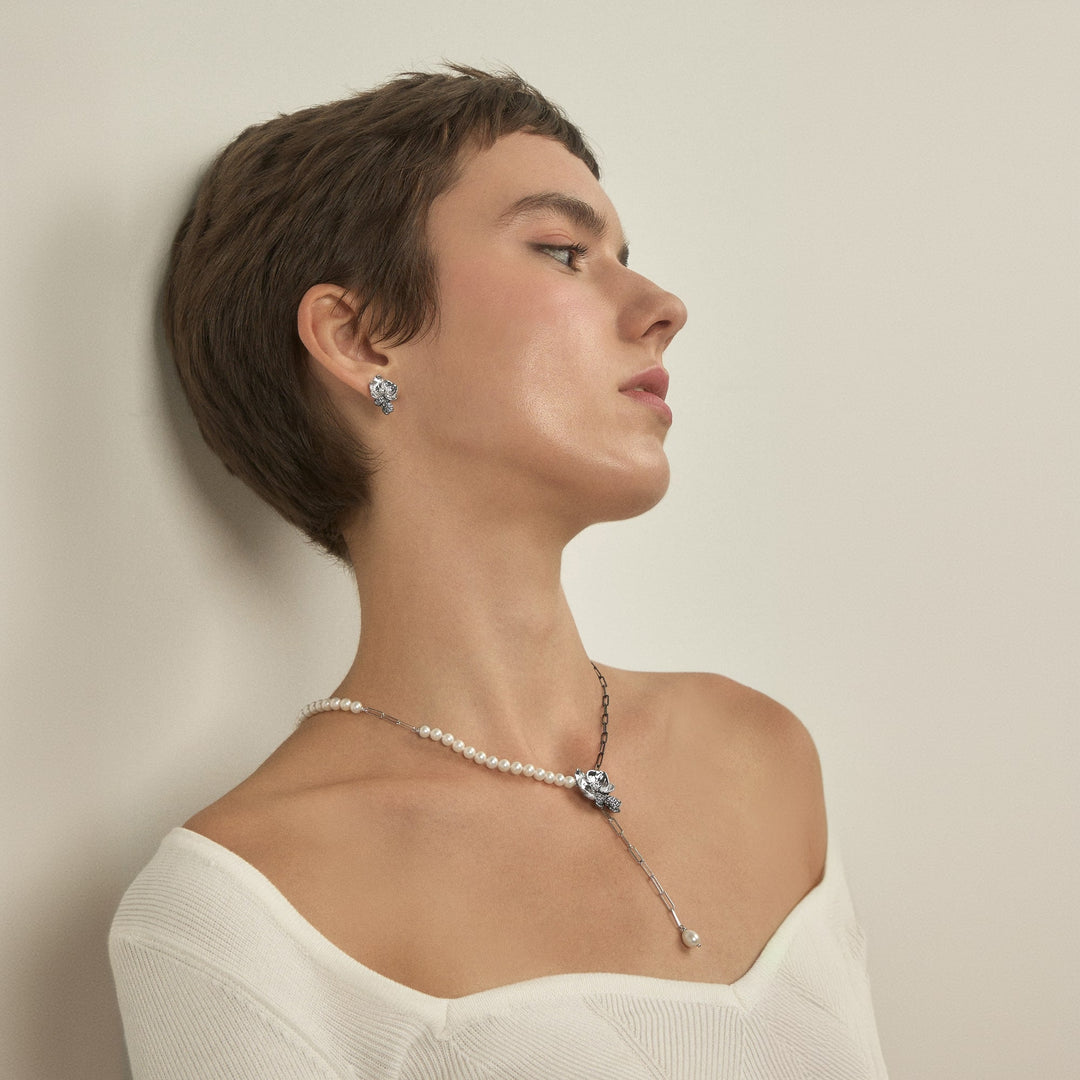 Risis Phalaenopsis Moments Necklace With Pearls - An elegant person showcases a pearl necklace with a sparkling pendant and matching earrings. The jewelry exudes classic beauty and sophisticated design with its silvery tones.