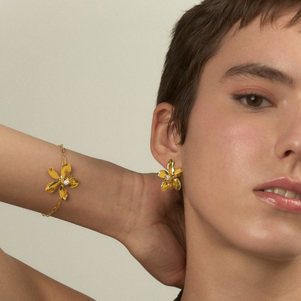 Risis Aeridovanda Blooms Bracelet - A person is wearing a golden bracelet and earring featuring shiny yellow orchid designs, highlighting elegance and beauty in a subtle fashion statement.